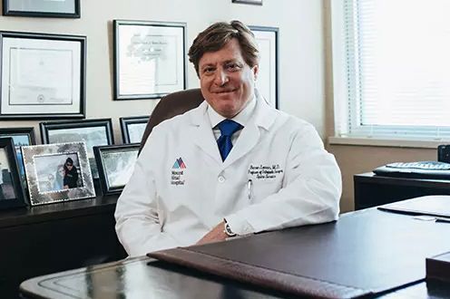 <p>Photo of a physician sitting behind a desk</p>
