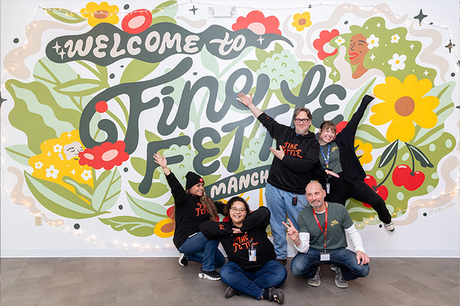 Fine Fettle employees posing in front of a mural that says "Welcome to Fine Fettle Manchester"