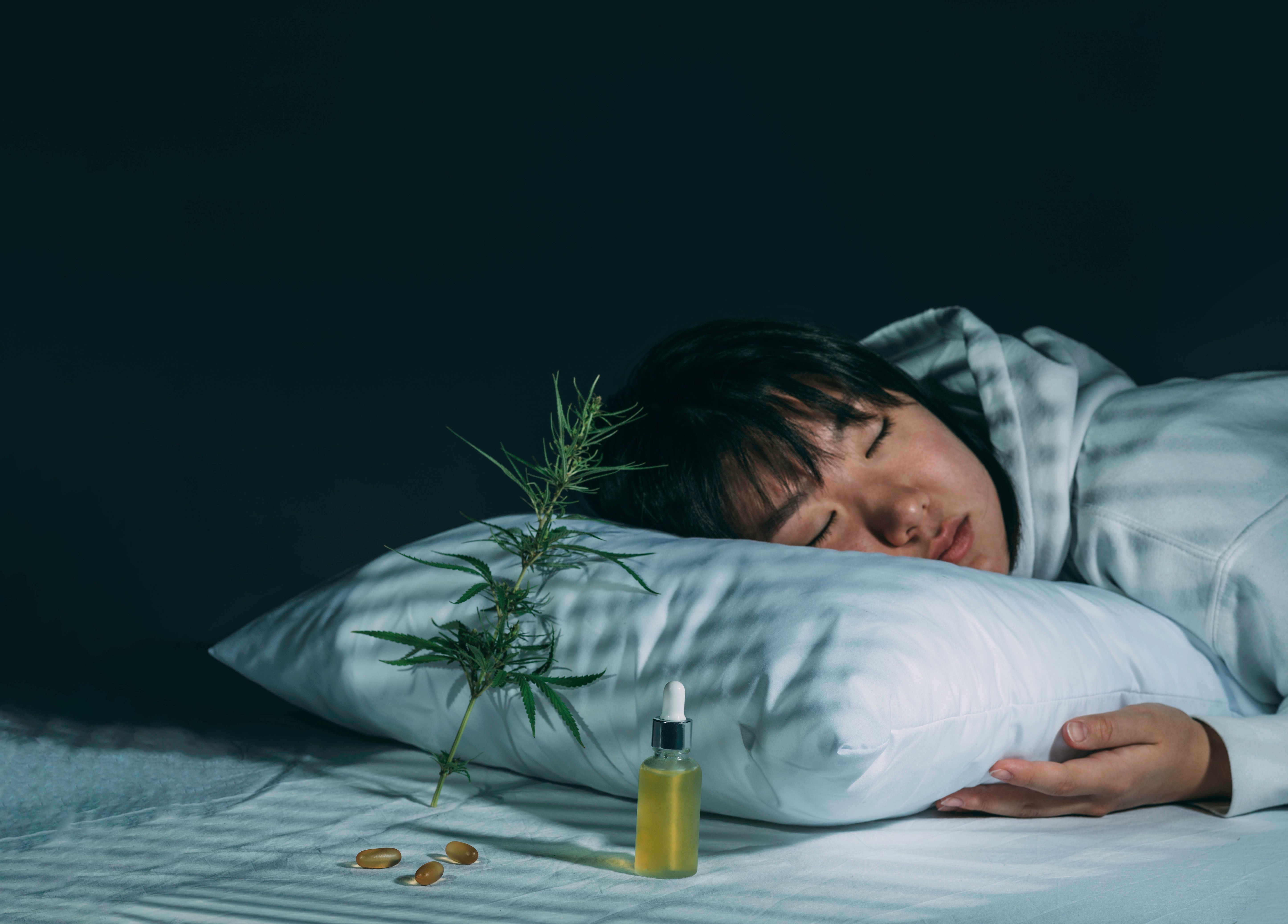 Person sleeping on pillow with cannabis oil, capsules, and cannabis branch