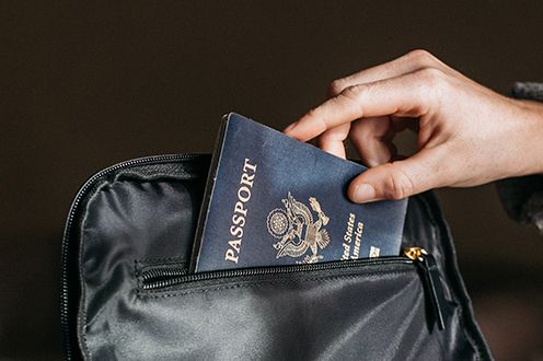 <p>Photo of a hand placing a passport into a handbag</p>
