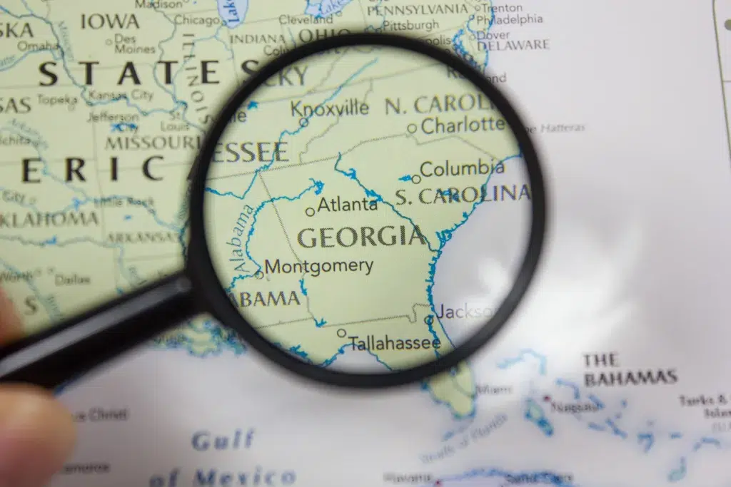 A magnifying glass focuses on the state of Georgia on a map of the southeastern United States, highlighting cities like Atlanta, Montgomery, and Tallahassee.