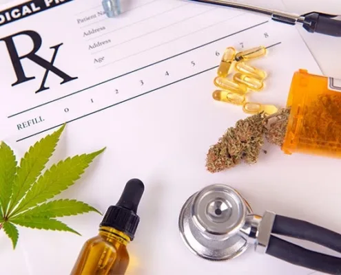A stethoscope, medical prescription form, cannabis leaf, cannabis bud, capsules, pill bottle, and a dropper bottle are arranged on a white surface.