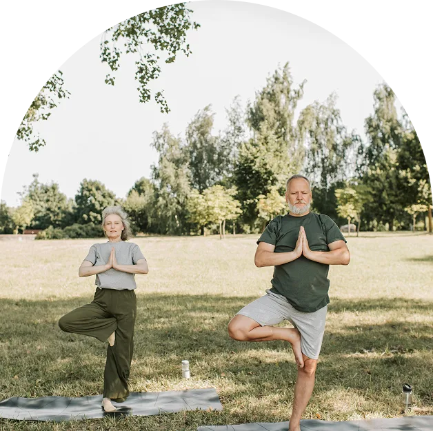 Two older adults practice yoga in a park, standing on mats in tree pose, surrounded by green grass and trees—reflecting a peaceful Georgia medical marijuana lifestyle.
