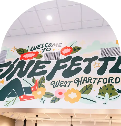 A mural on a wall at the cannabis dispensary reads Welcome to Fine Fettle West Hartford, featuring colorful flowers, leaves, stars, and red sneakers in the design.
