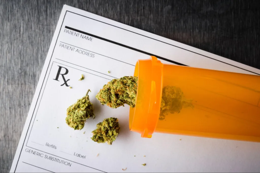 Prescription bottle with cannabis buds spill over a prescription form.