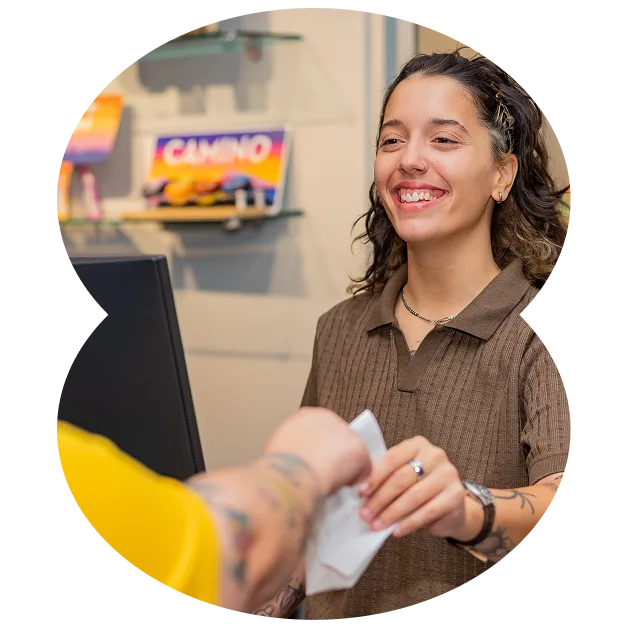 A smiling cashier hands a receipt to a customer across the counter in a brightly lit cannabis delivery store.