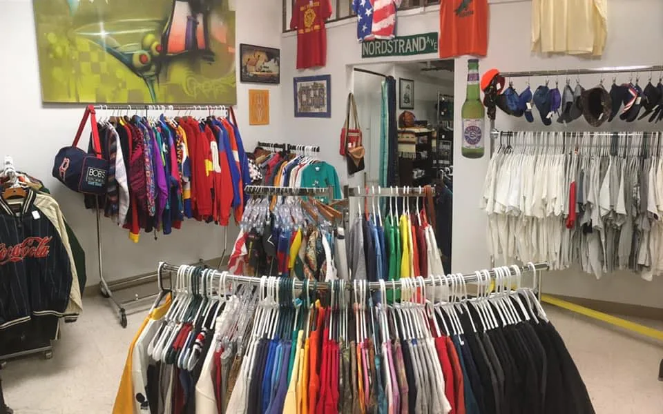 Interior of a vintage clothing store with colorful shirts and jackets on racks, hats on a wall, and various decorations and signs hanging around the room.