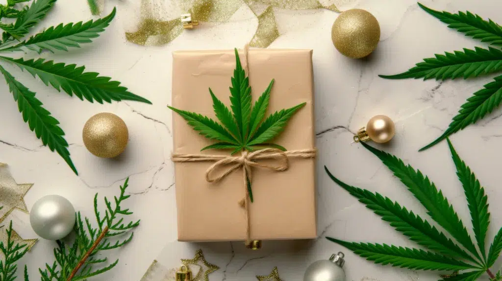 A wrapped gift box decorated with a cannabis leaf and twine, surrounded by gold ornaments and cannabis leaves on a marble surface.