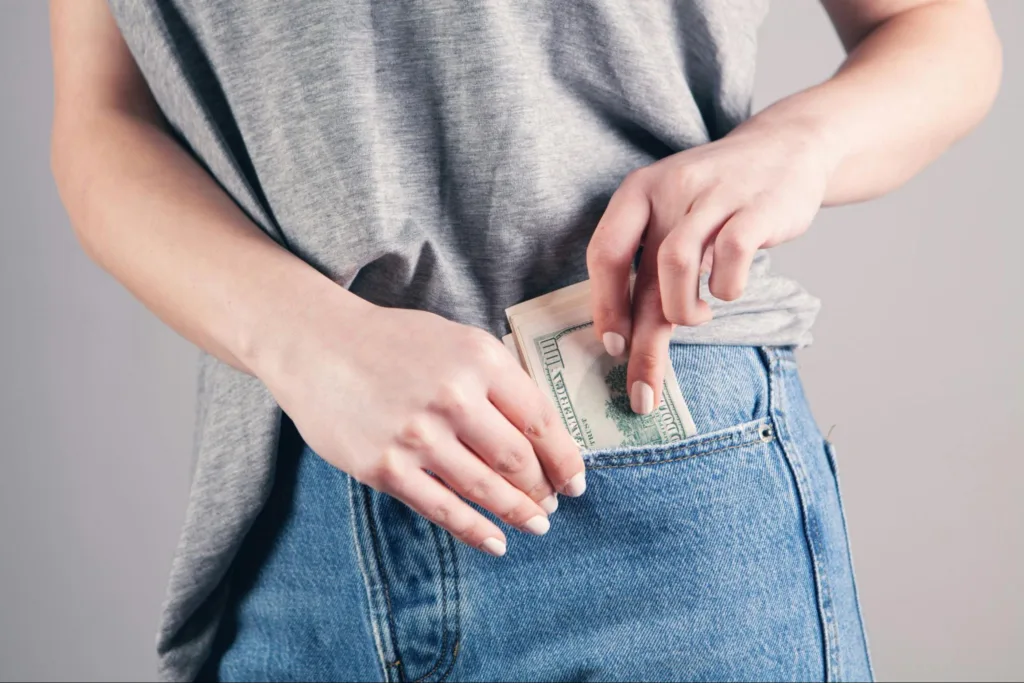 A person slipping a wad of cash into their pants pocket.