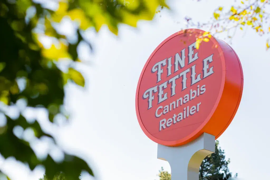 A round orange sign for Fine Fettle Cannabis Retailer mounted on a pole.